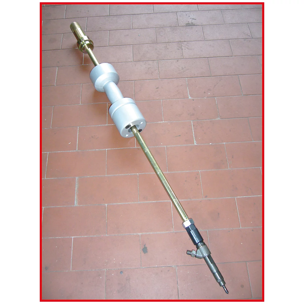 Ein Werkzeug auf einem braunen Fliesenboden. Das Werkzeug hat eine zylindrische Form mit verschiedenen Metallabschnitten.